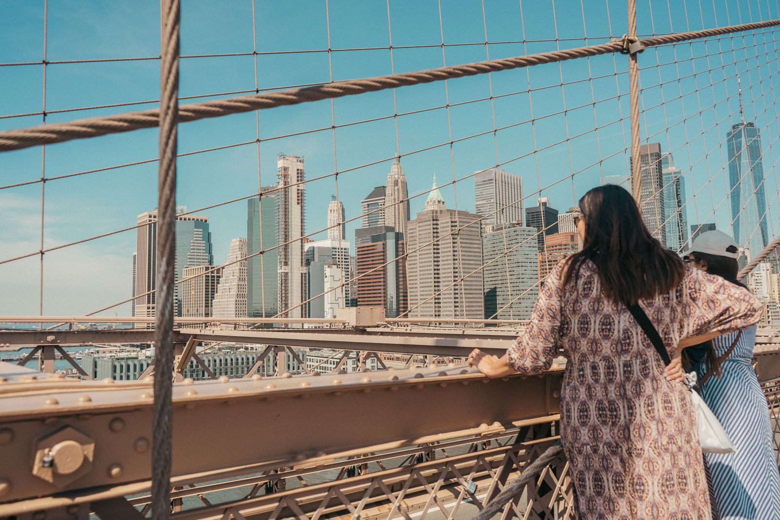 Two women enjoy the view of Manhattan skyline from Brooklyn Bridge, NYC.