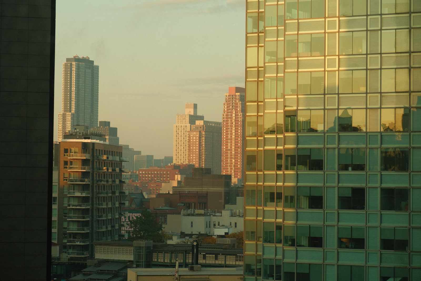 View of New York City's skyline at dawn with reflections on modern buildings.
